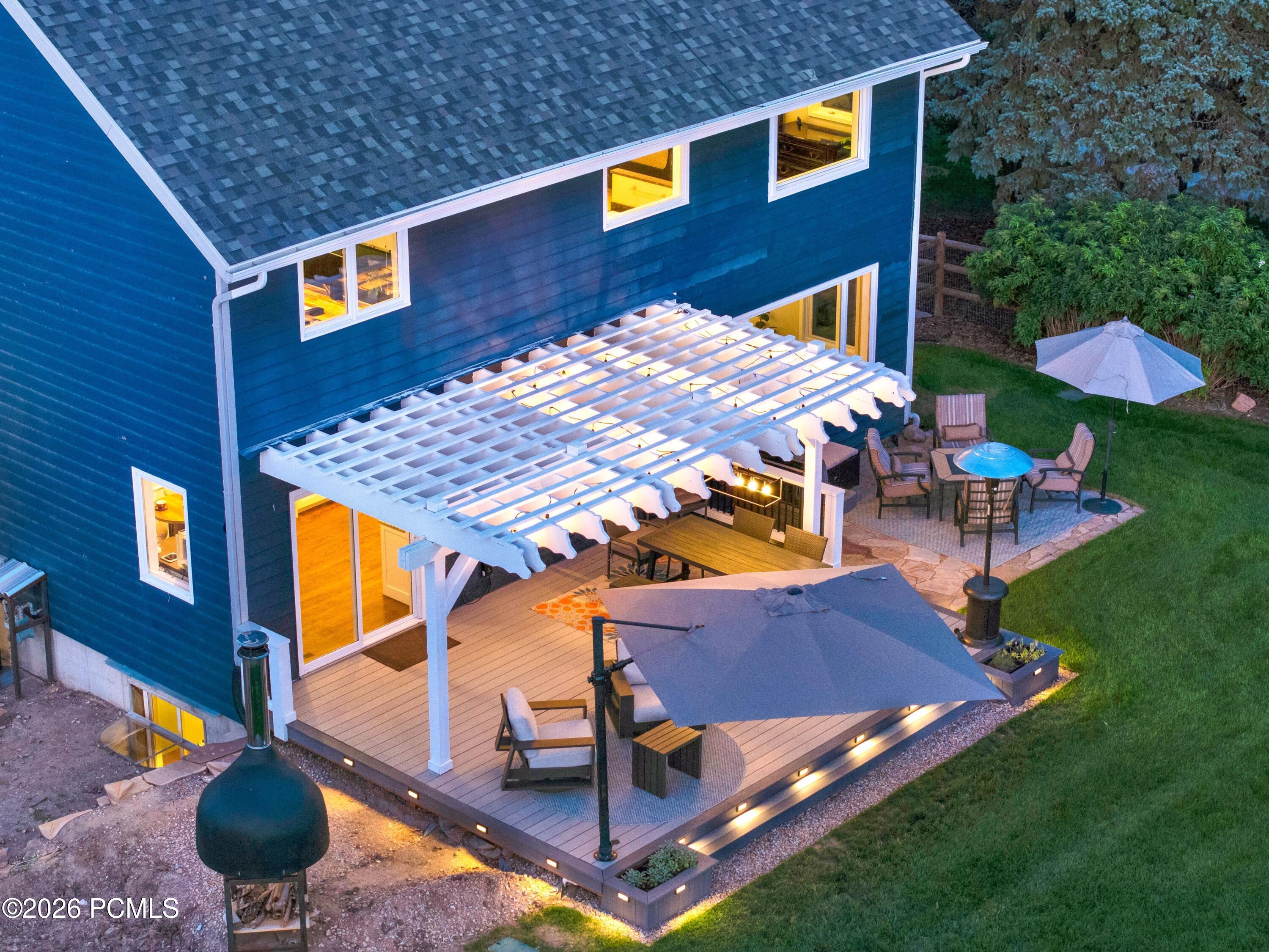 Blue two-story home with an illuminated deck, white pergola, and outdoor dining and lounge areas.