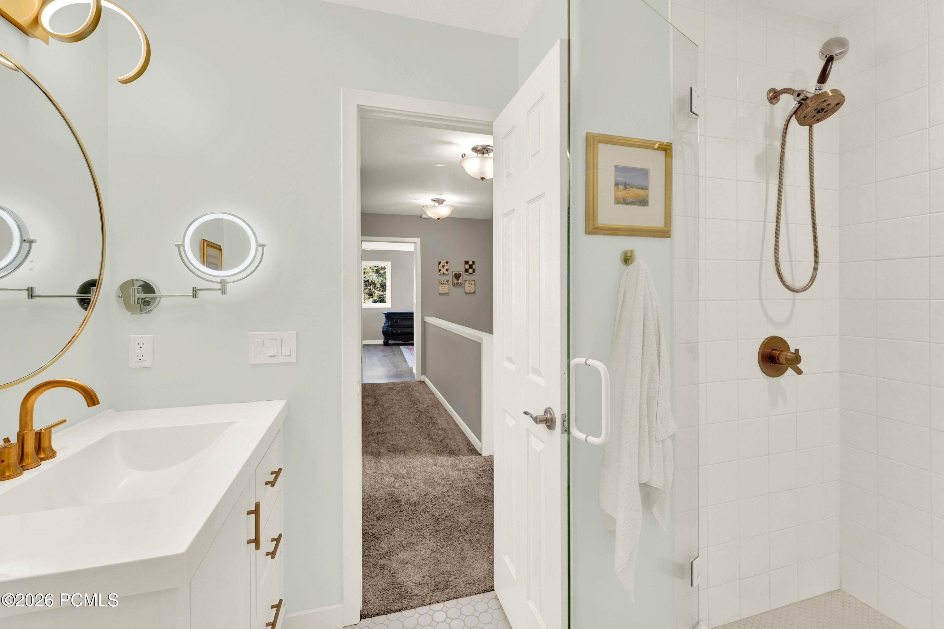 Bathroom with a white vanity and glass shower featuring bronze fixtures and white tile.