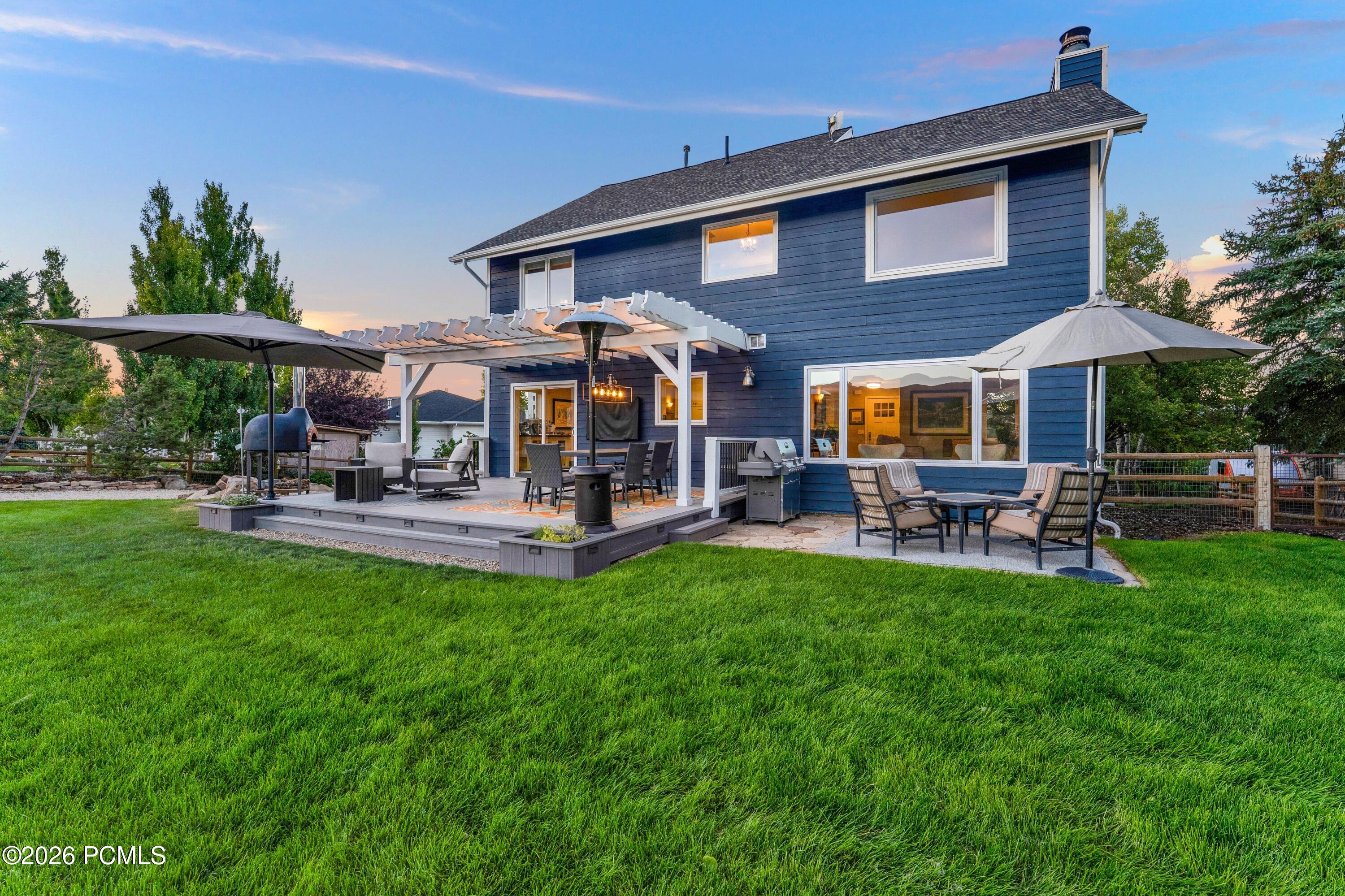Blue two-story home with a pergola-covered patio, outdoor seating, and a wide green lawn at dusk.