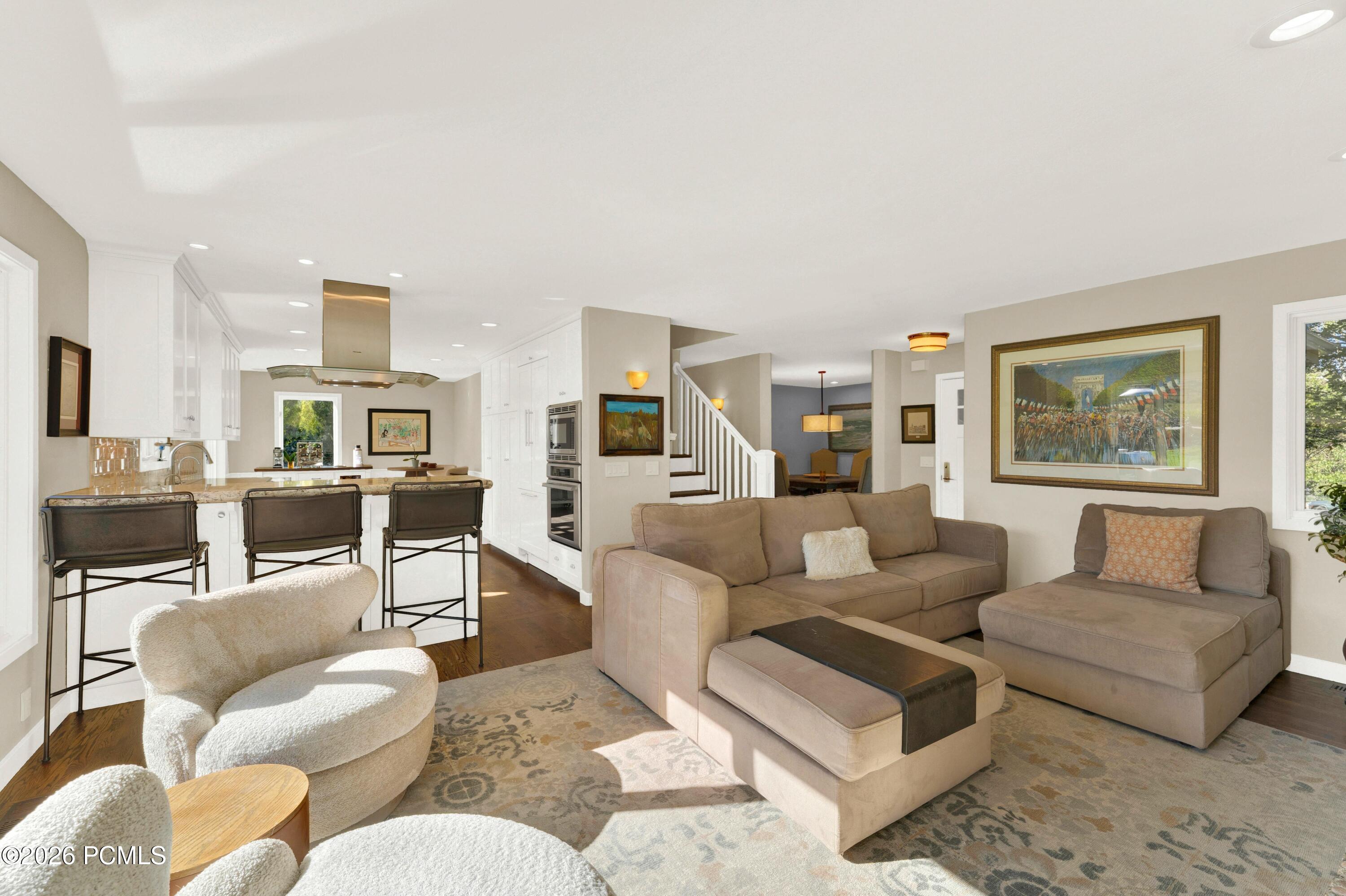 Open-plan living room and kitchen with taupe seating, white cabinetry, and a kitchen island with bar stools.