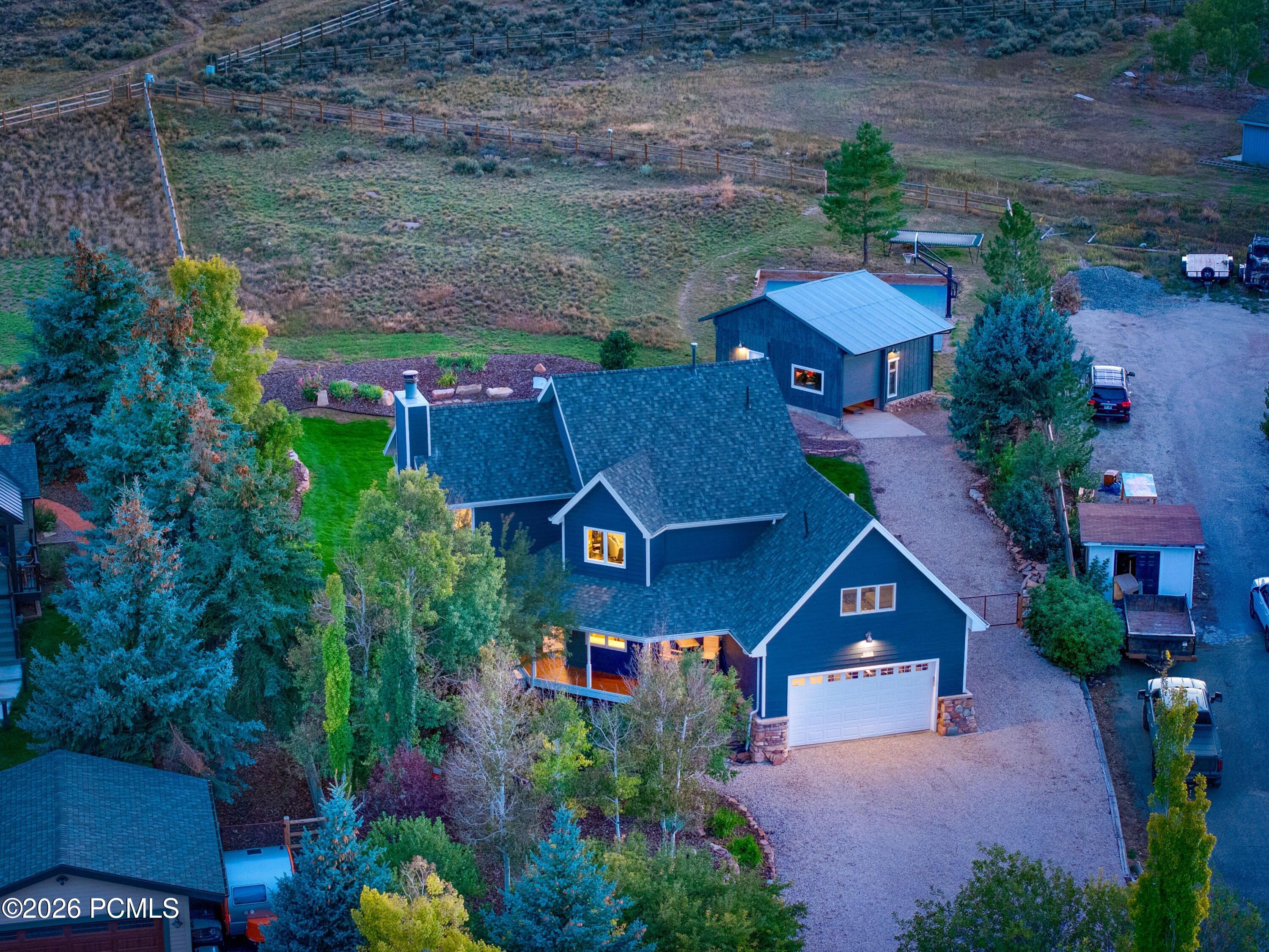 Blue house with white garage and gravel drive, viewed from above at dusk with a detached outbuilding.
