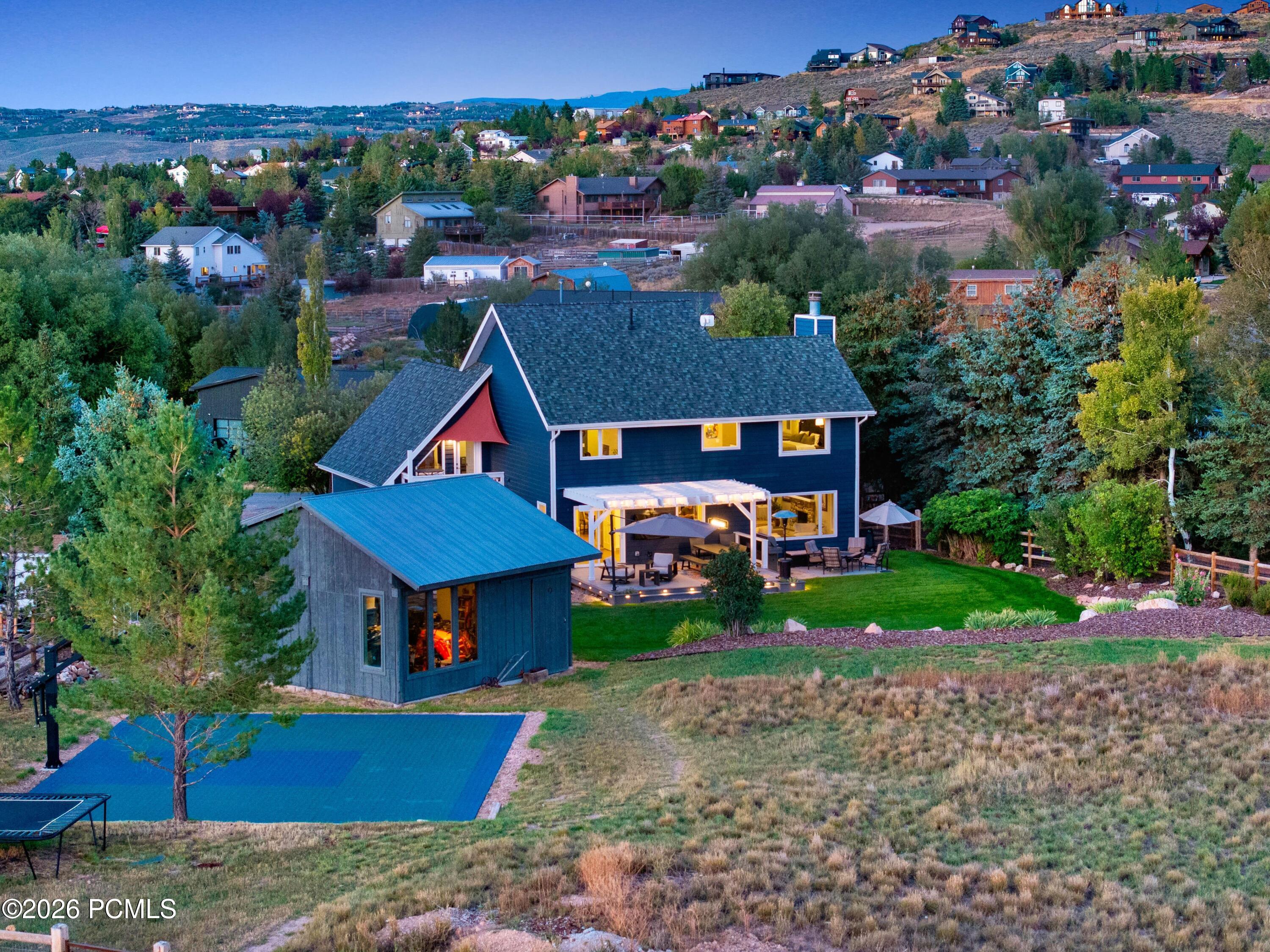 Dark blue two-story home with illuminated windows, covered patio, landscaped yard, and rectangular pool.
