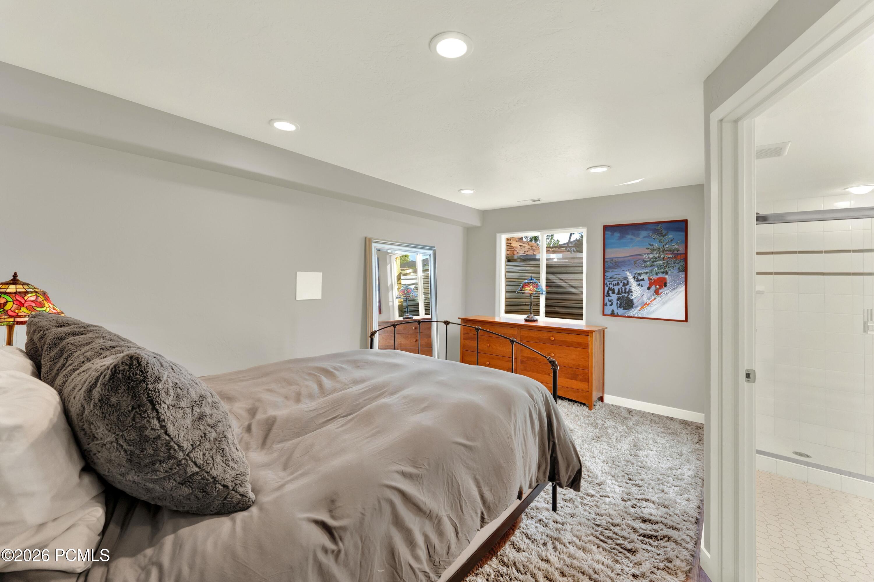 Furnished bedroom with a gray bed, wooden dresser, shag carpet, and adjoining tiled shower.