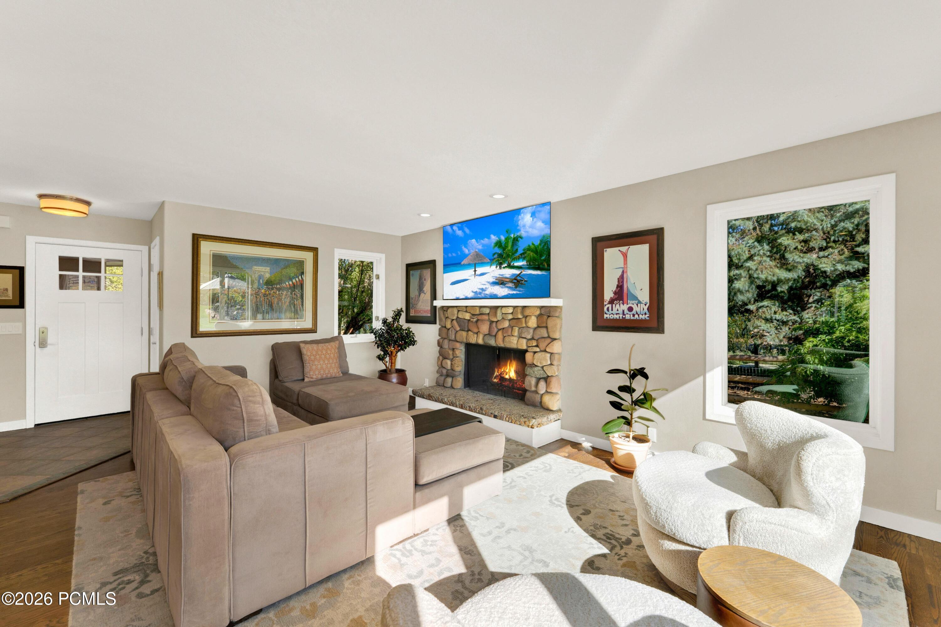 Living room with a rounded stone fireplace, sectional sofa, and sunlit window overlooking evergreen trees.
