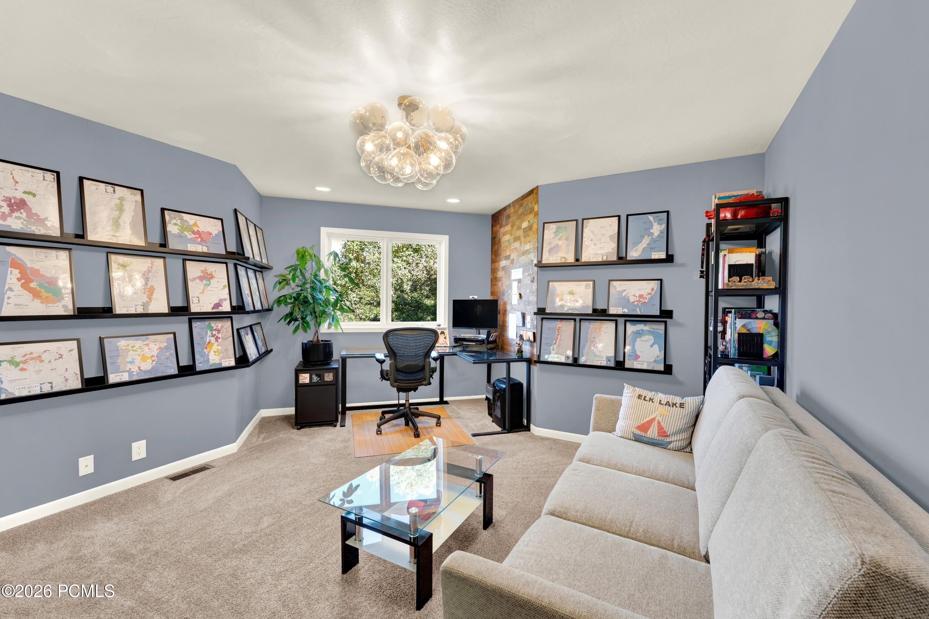 Home office with framed maps, a desk by the window, and a light-colored sectional sofa.