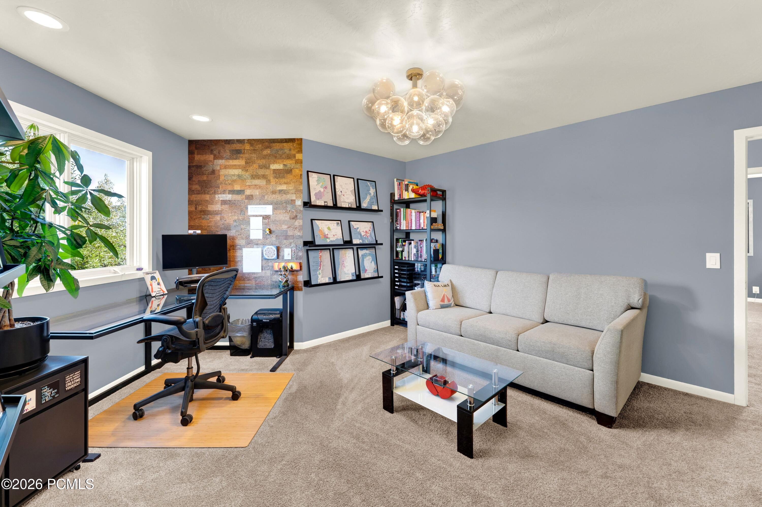 Home office and sitting room with a desk by the window, framed maps, and a gray sofa.