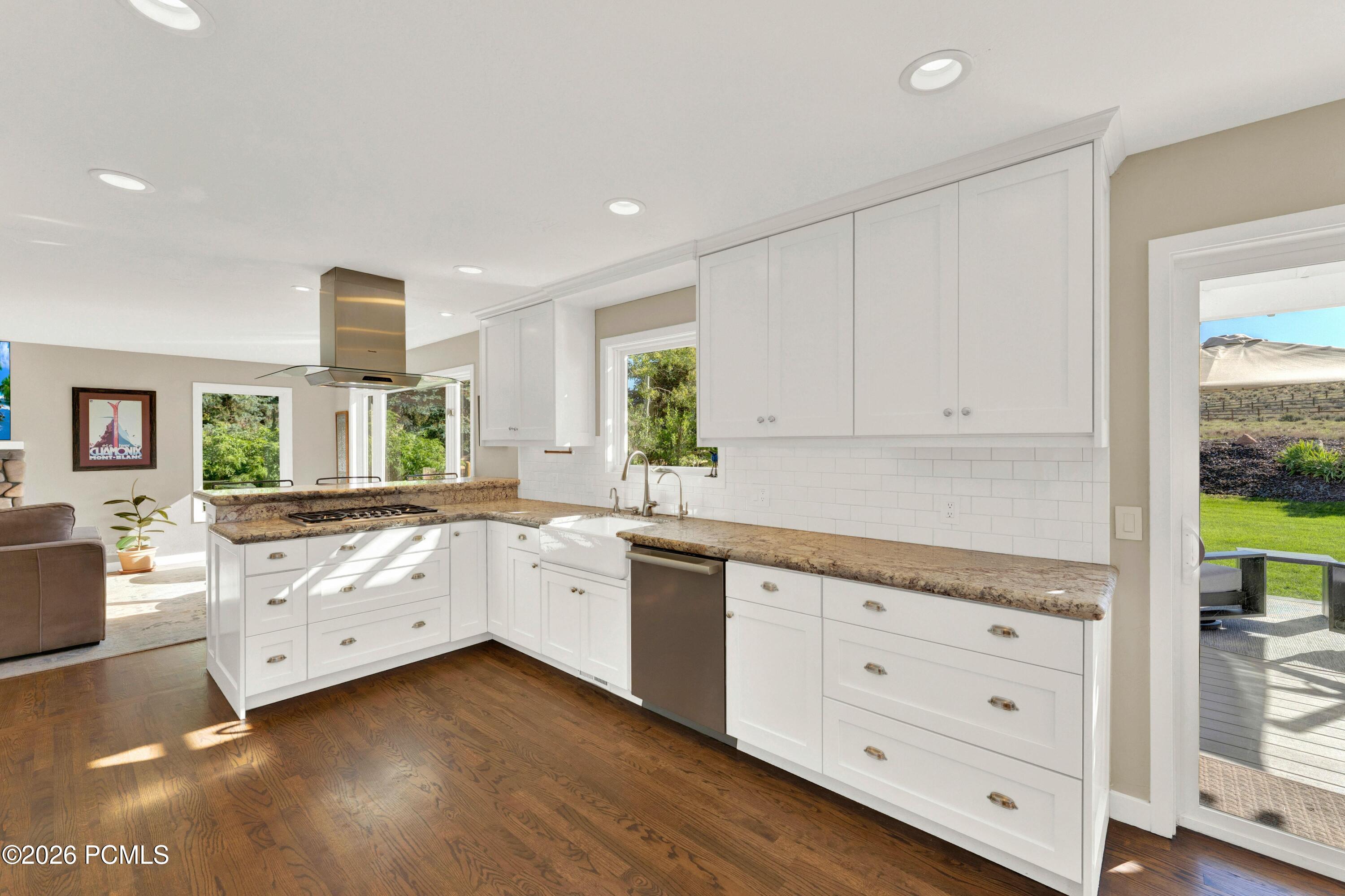 Bright kitchen with white cabinets, granite counters, a farmhouse sink, and hardwood floors.