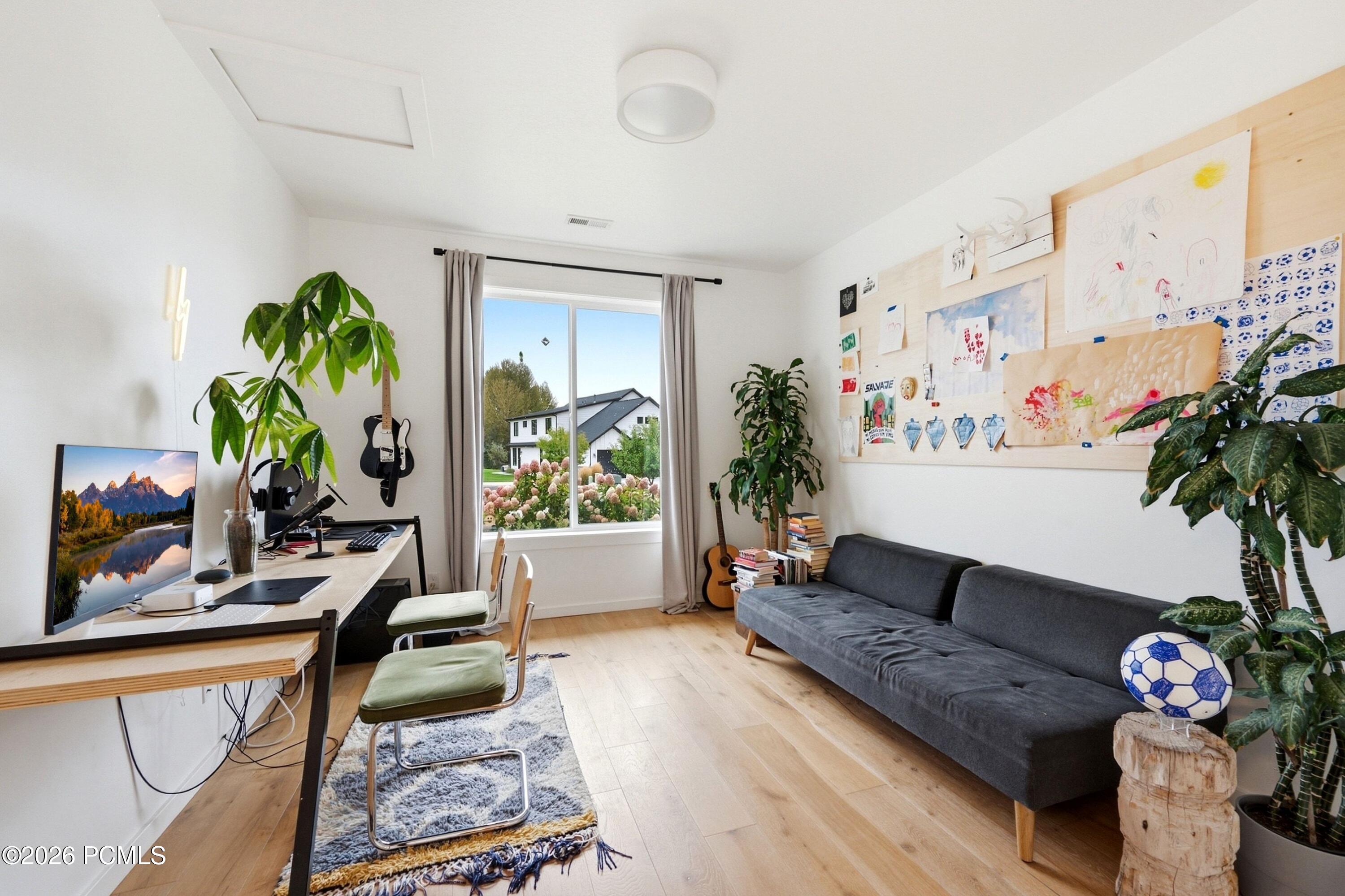 Home office and sitting room with a desk, gray sofa, guitars, and children's artwork.