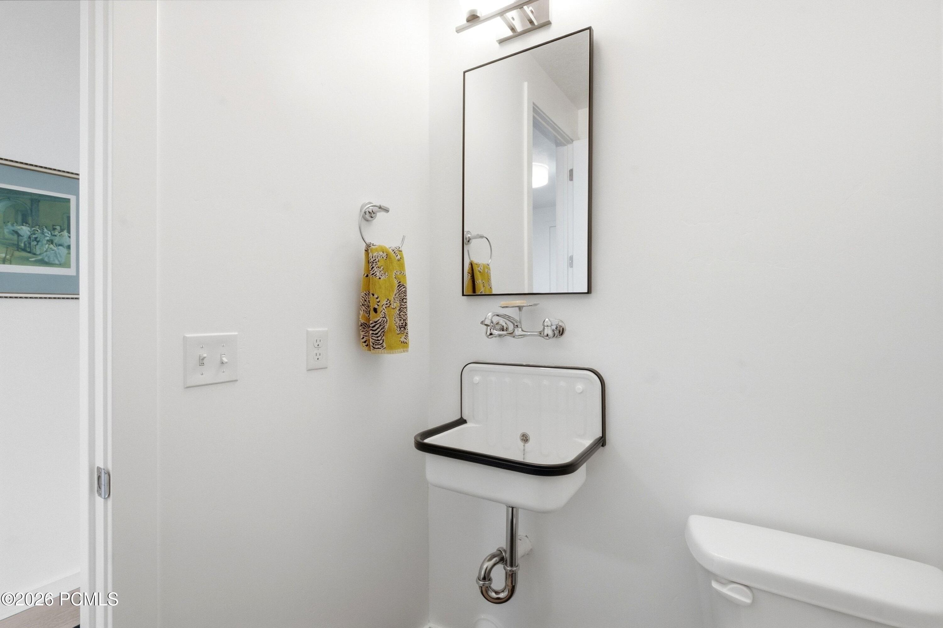 Bright white bathroom with a wall-mounted porcelain sink, black trim, chrome faucet, and yellow patterned towel.