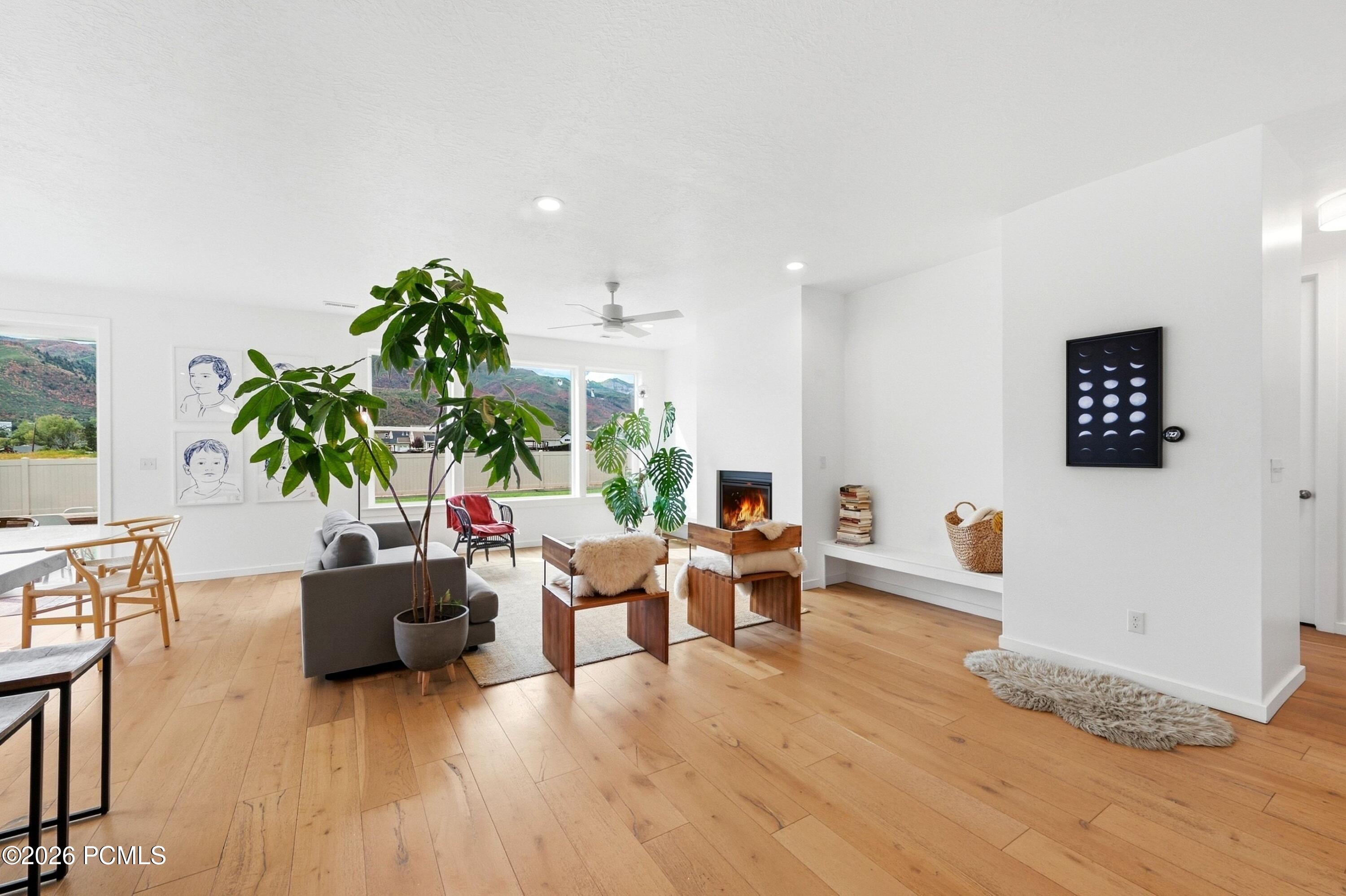Living room with a lit fireplace, large windows, mountain views, and light wood floors.