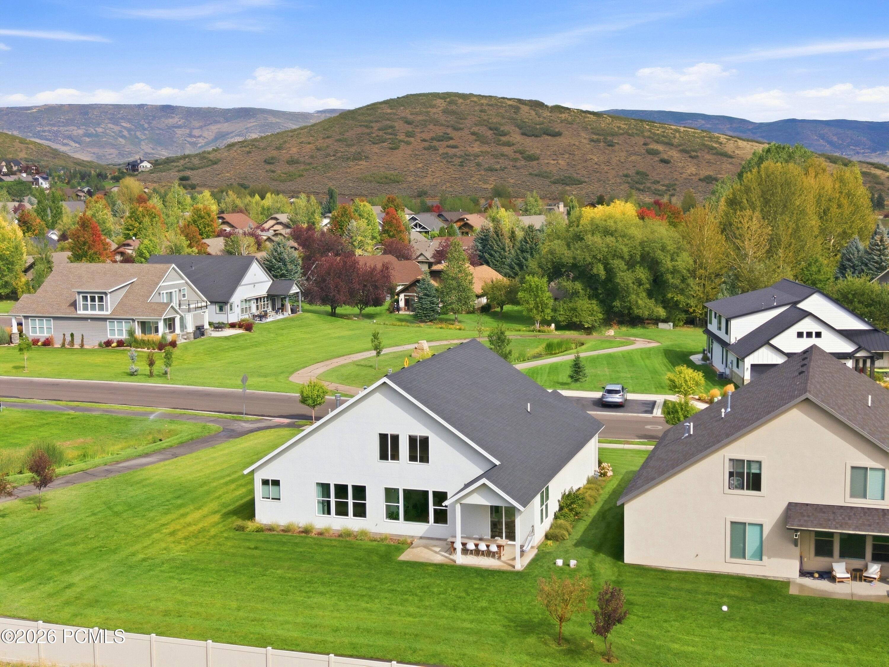 Aerial view of a white home and neighboring houses amid autumn trees, with a hillside and mountains beyond.