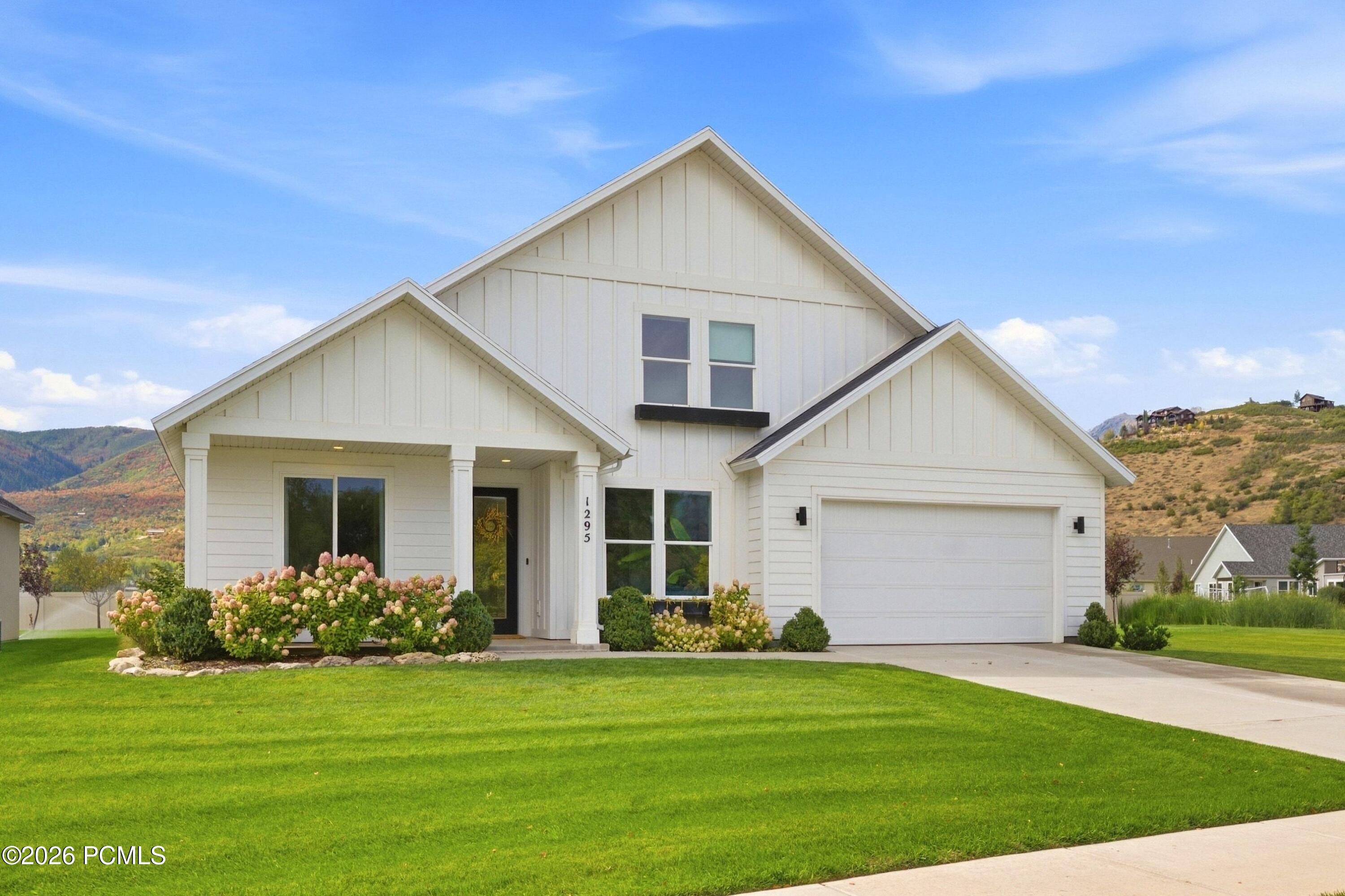 White two-story home with a covered entry, two-car garage, flower beds, and green lawn.