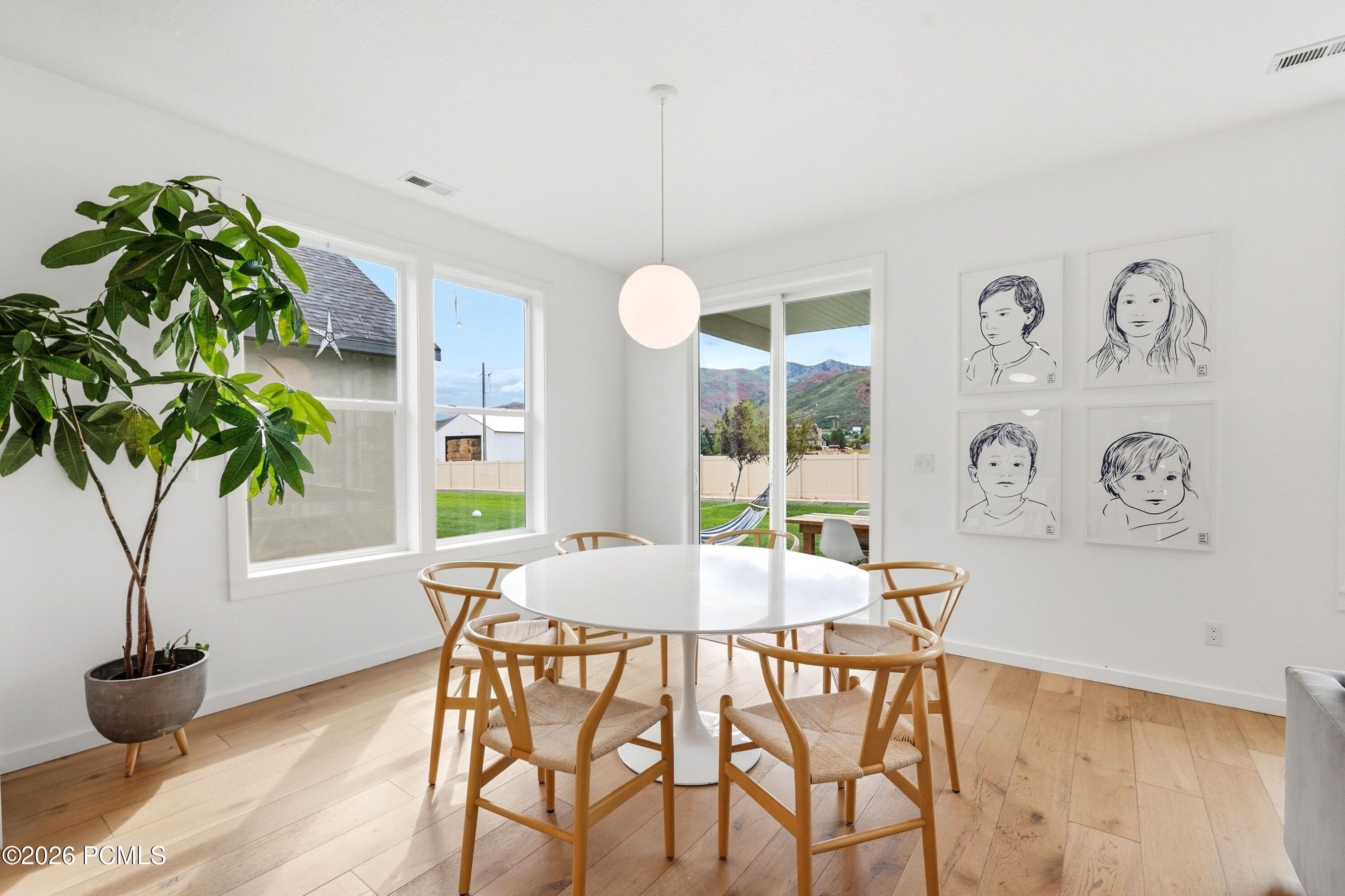 Dining room with a round white table, framed portraits, and mountain views through large windows.