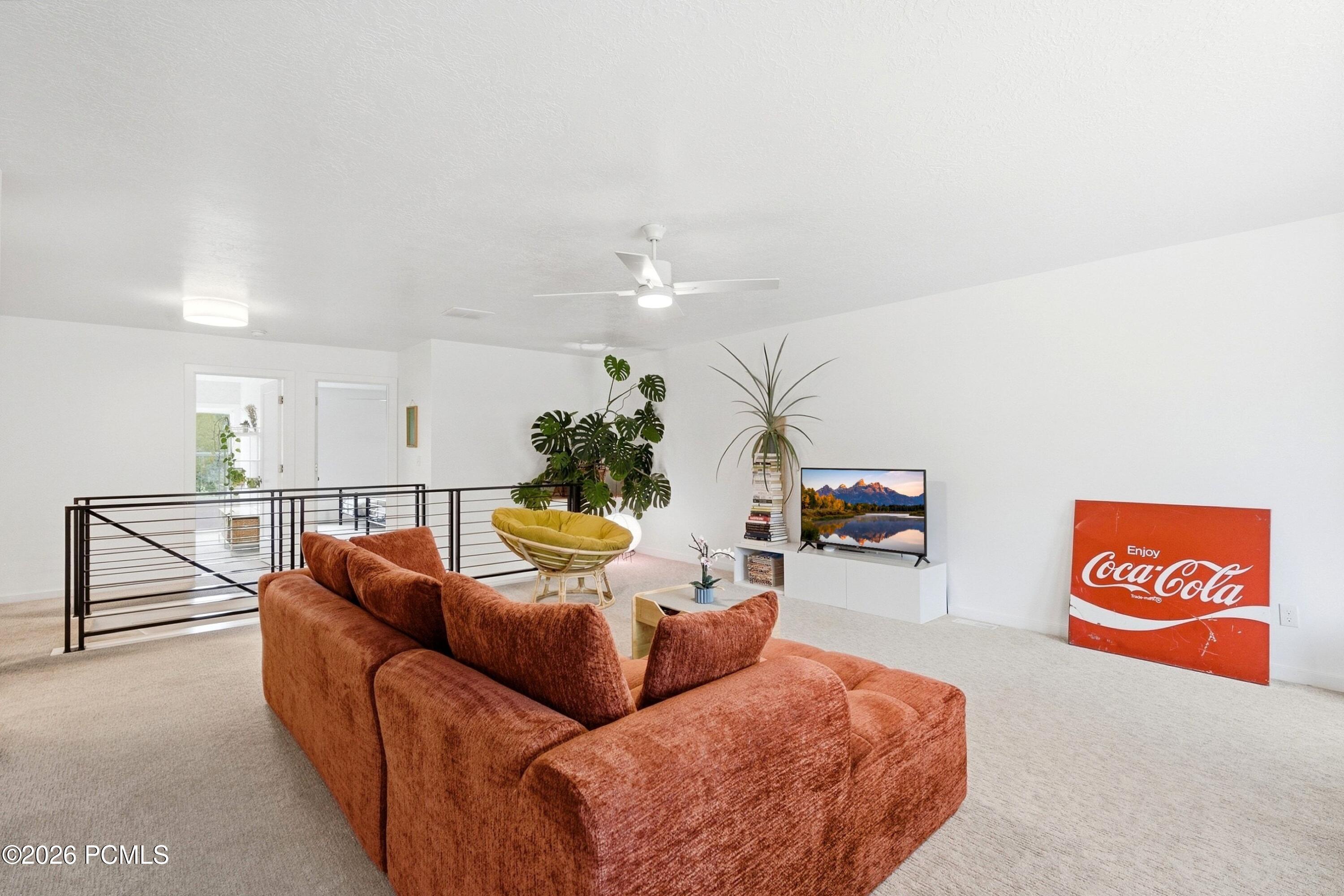 Upstairs living room with a rust-colored sectional, yellow chair, leafy plants, and black metal railing.