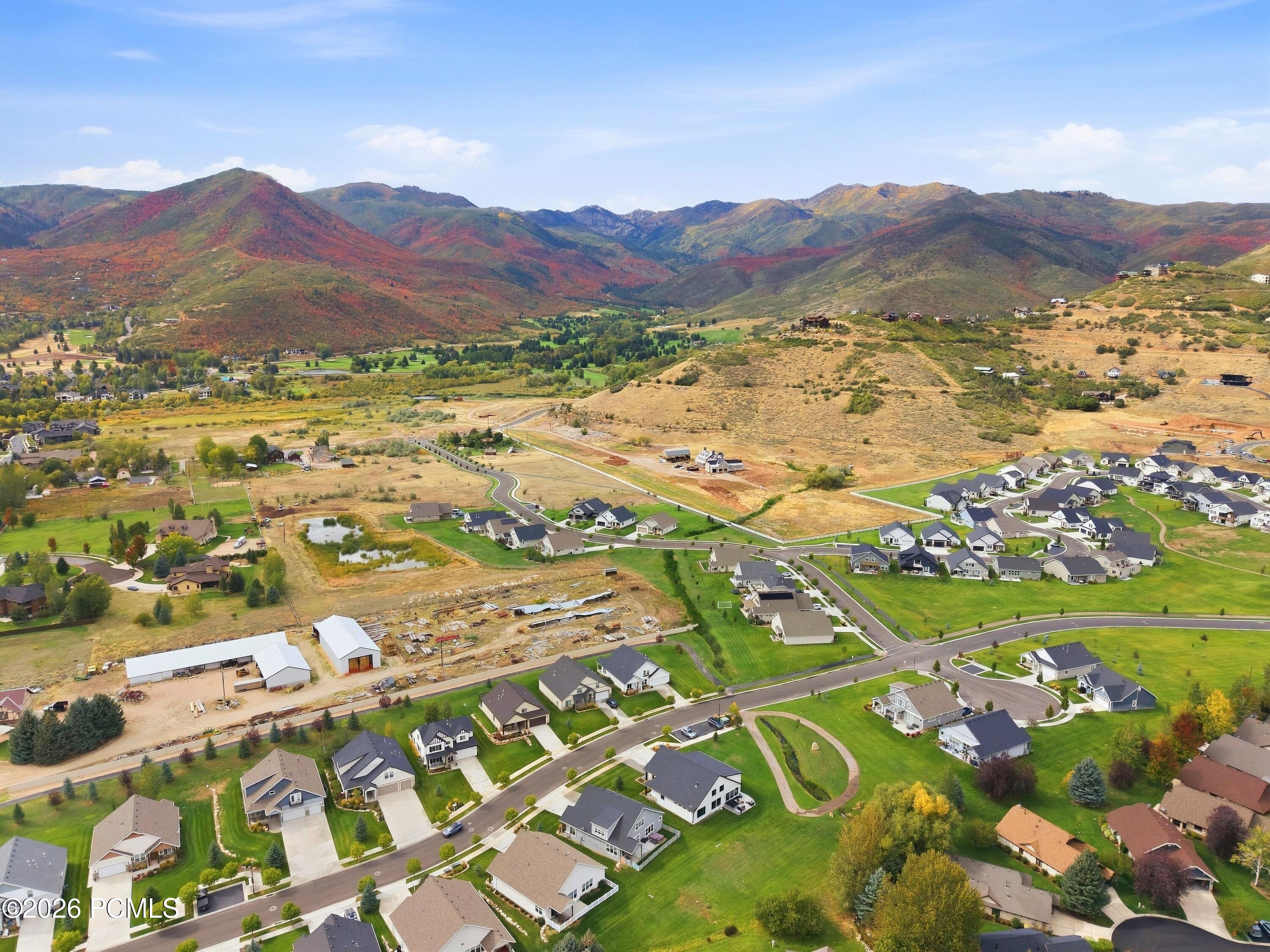 Aerial view of a residential neighborhood and open land beneath colorful autumn mountains.