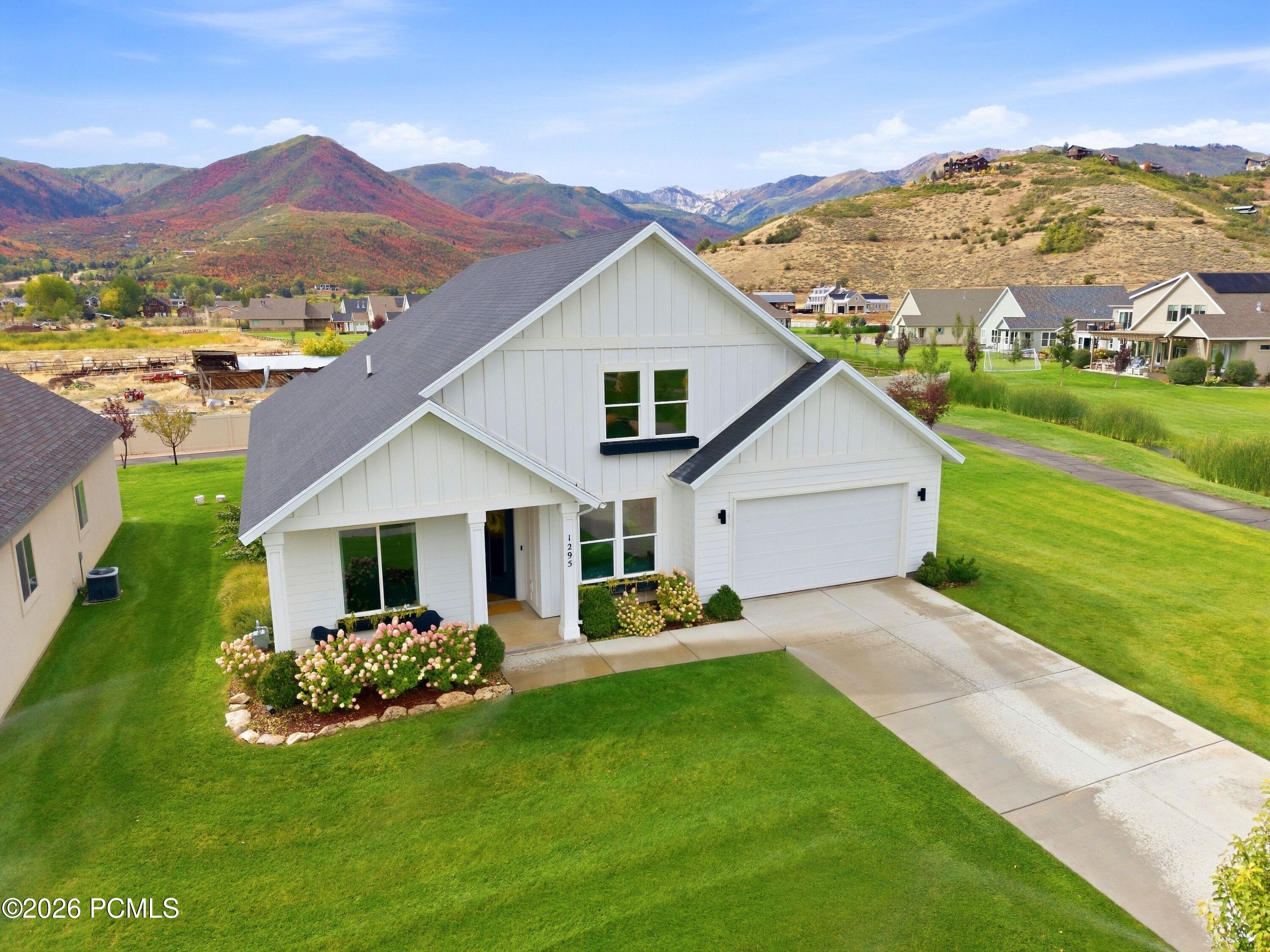 White two-story home with attached garage, flowering front garden, and autumn mountain views.