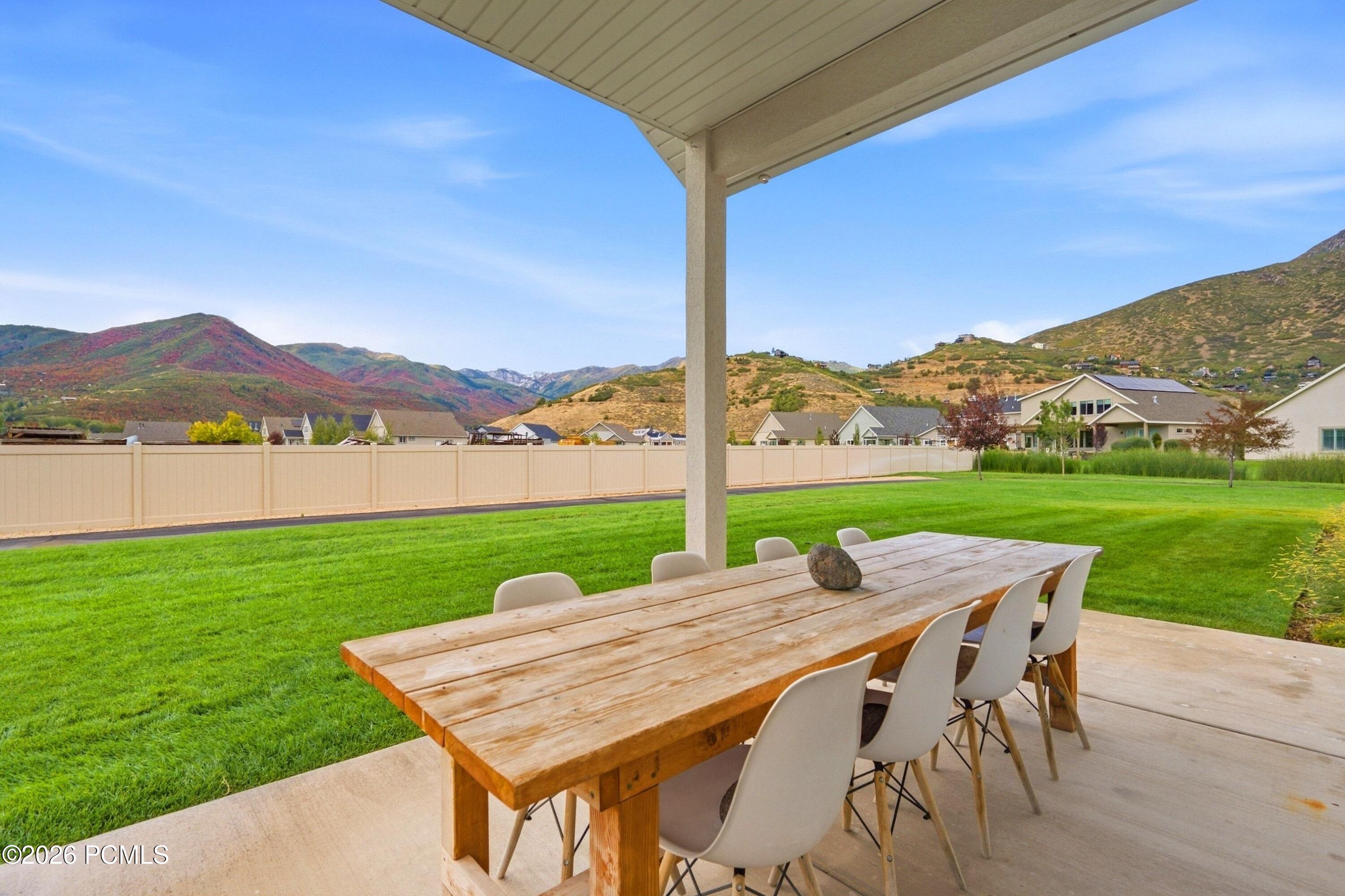 Covered patio dining table overlooking a green lawn and autumn-colored mountains.