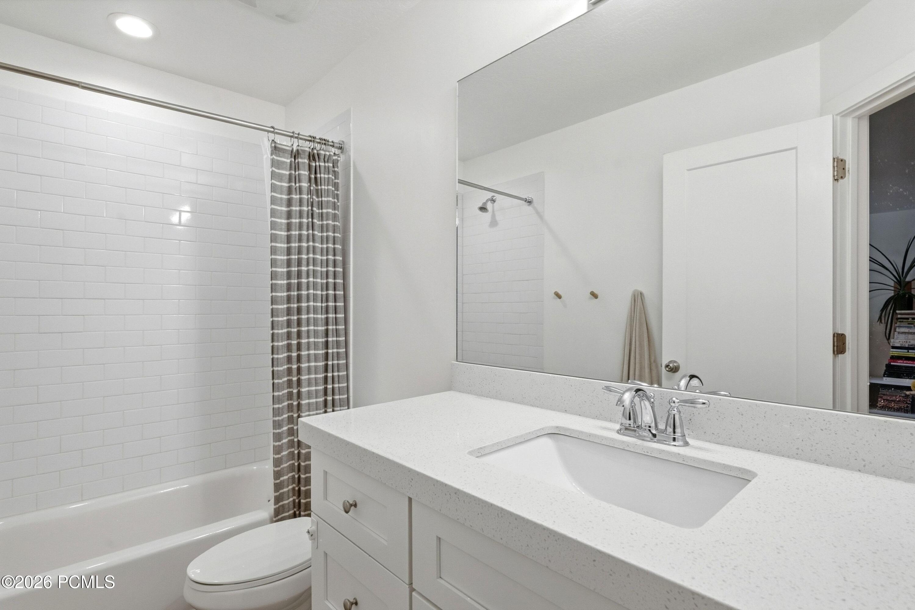 Bathroom with a subway-tile tub surround, striped shower curtain, and white vanity with an integrated sink.