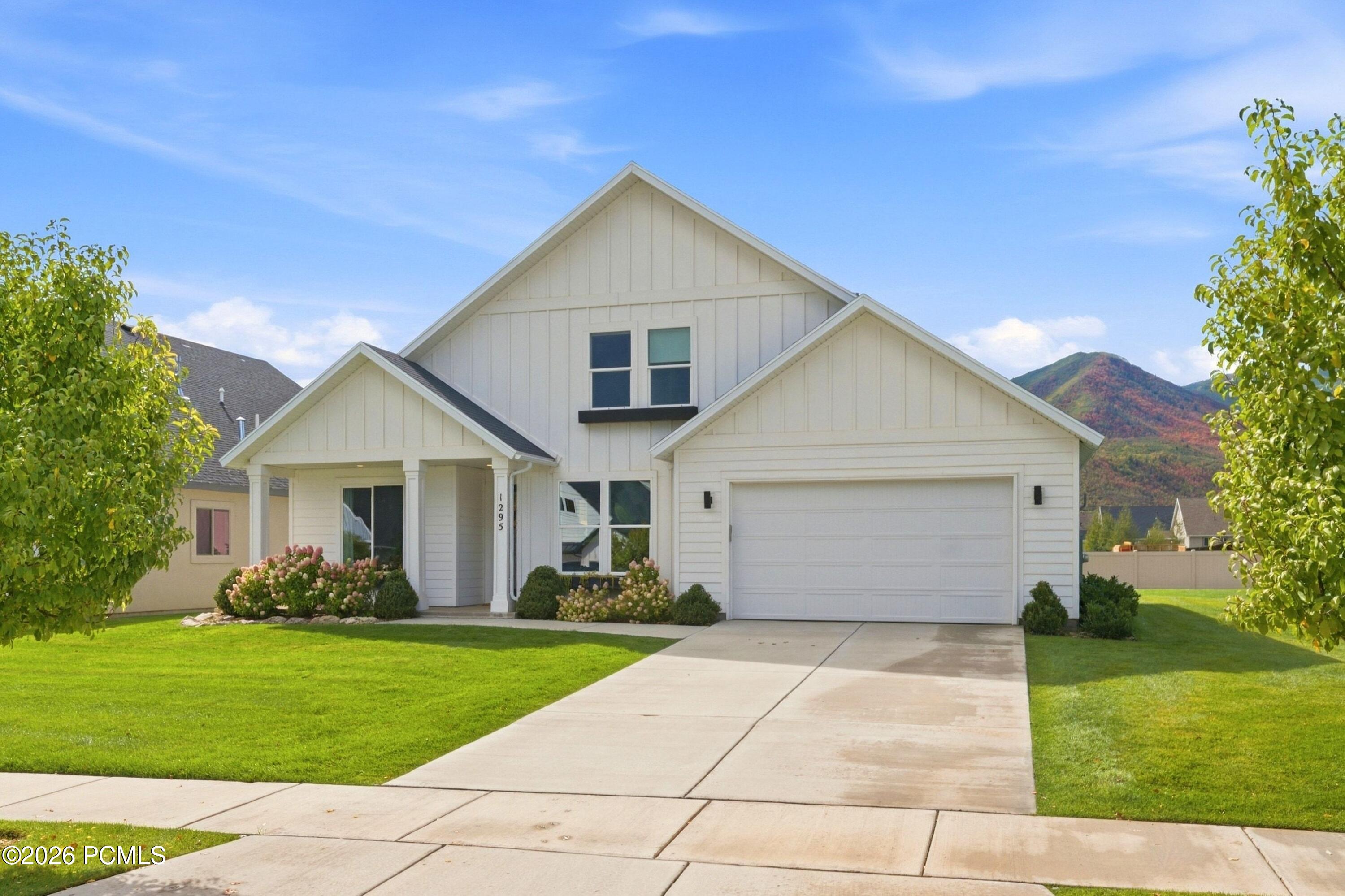 White two-story home with a double garage, landscaped lawn, and autumn-colored mountain behind it.