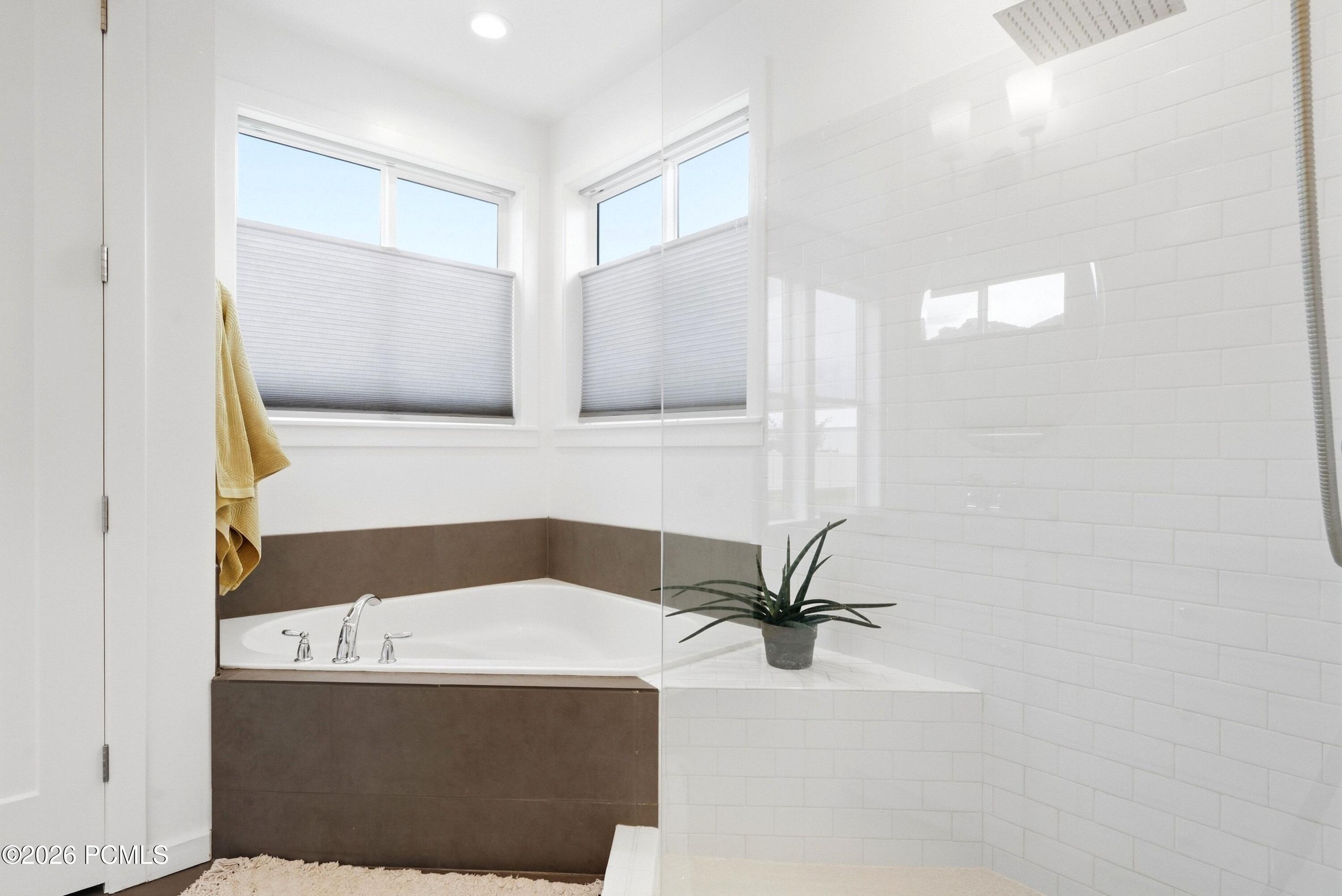 Bright bathroom with a corner soaking tub and glass-enclosed shower lined with white subway tile.