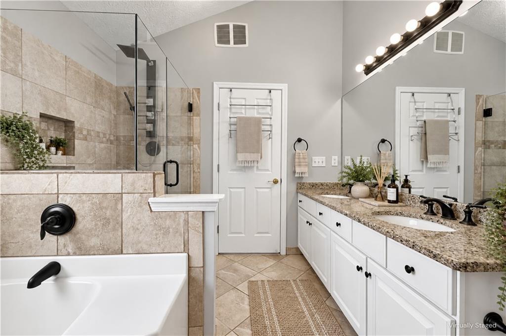 Bathroom with a tiled glass shower, bathtub, and long double vanity with granite countertops.