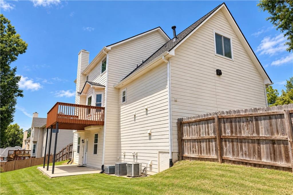 Rear of a light-colored two-story house with a raised deck, patio, and fenced lawn.