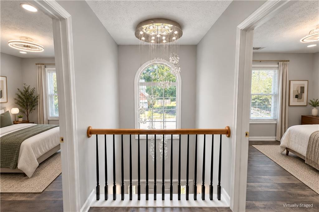 Upstairs landing with an arched window and cascading chandelier, between two furnished bedrooms.
