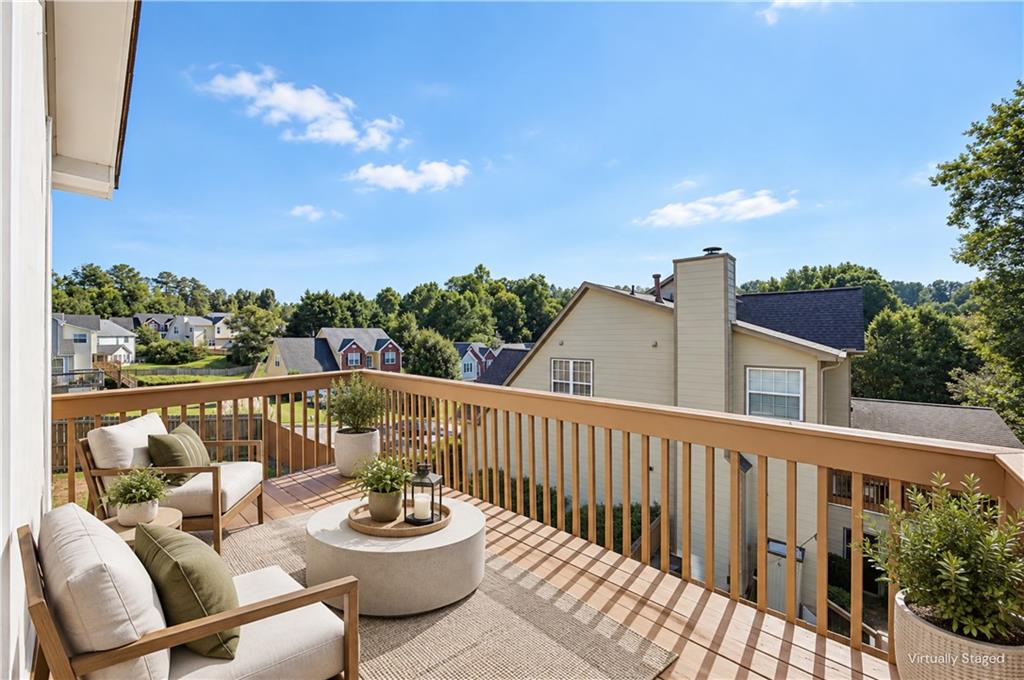 Furnished deck overlooking neighboring homes and trees, with cushioned chairs and a round coffee table.