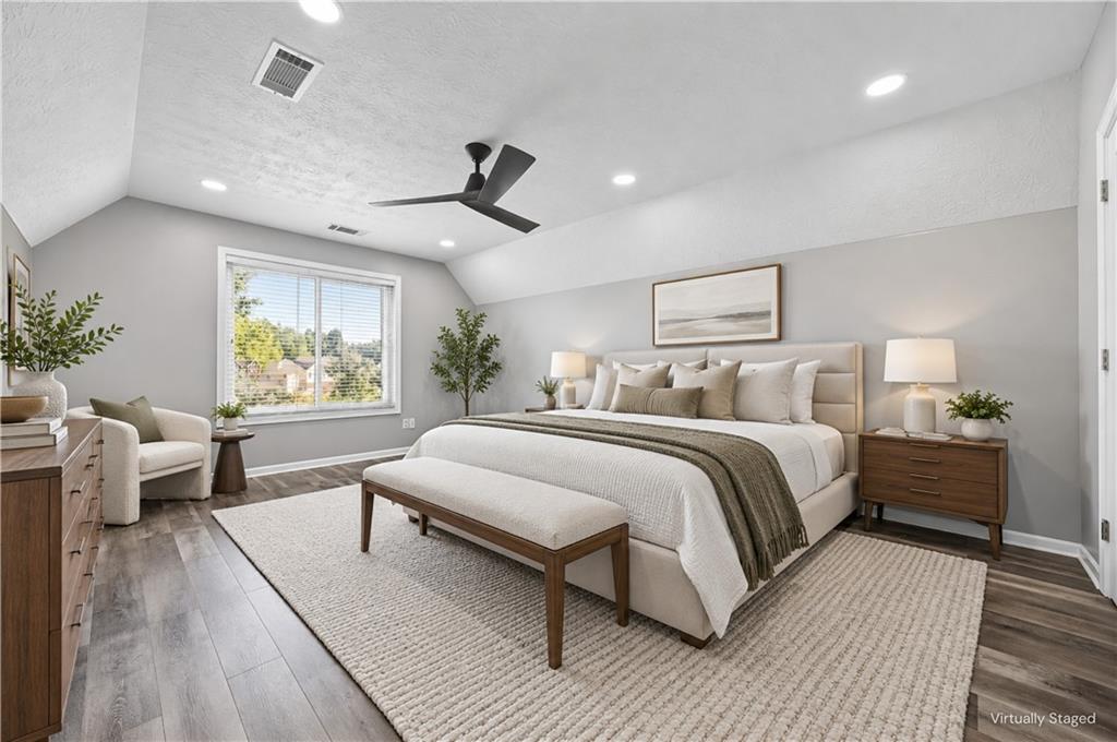Virtually staged bedroom with a large upholstered bed, bench, ceiling fan, and window overlooking trees.