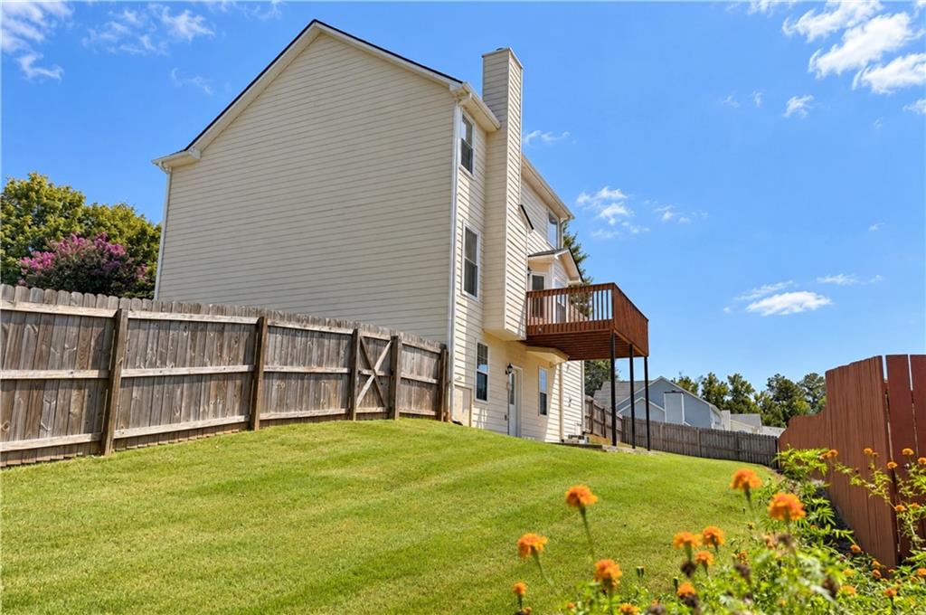 Beige two-story house with a raised deck overlooking a sloped lawn enclosed by wooden fences.