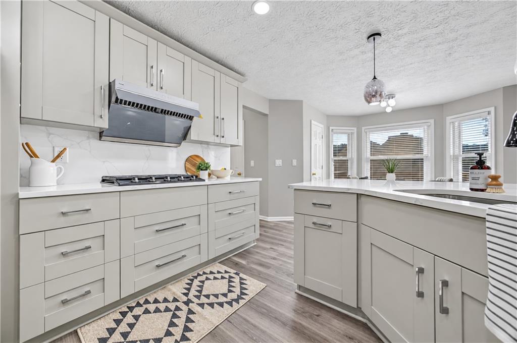 Kitchen with pale gray cabinets, marble-look backsplash, gas cooktop, and a large island.