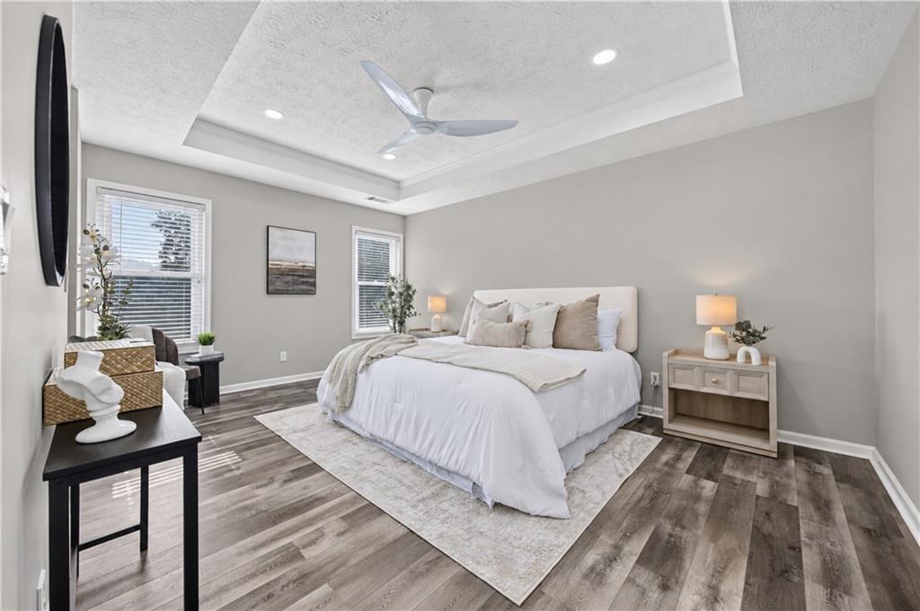 Bedroom with a king-size bed, tray ceiling, ceiling fan, and wood-look flooring.