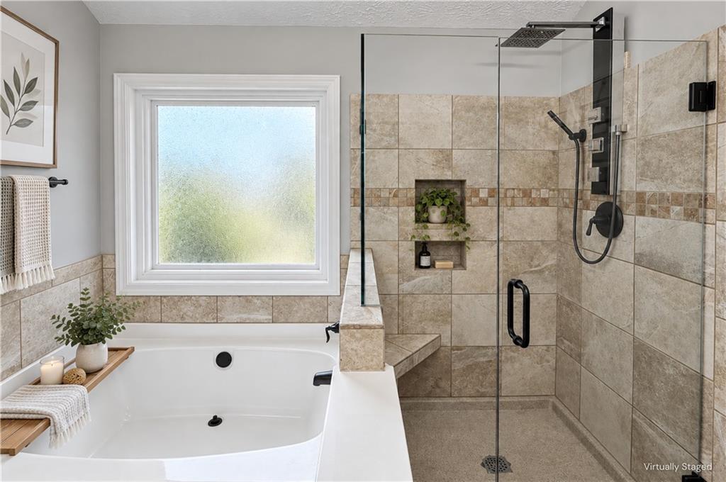Bathroom with a soaking tub beside a glass-enclosed, tiled shower and frosted window.
