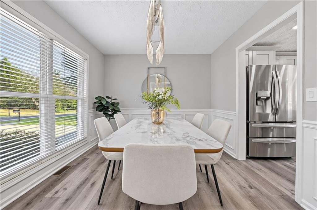 Dining room with a marble-look table, upholstered chairs, and large windows overlooking greenery.