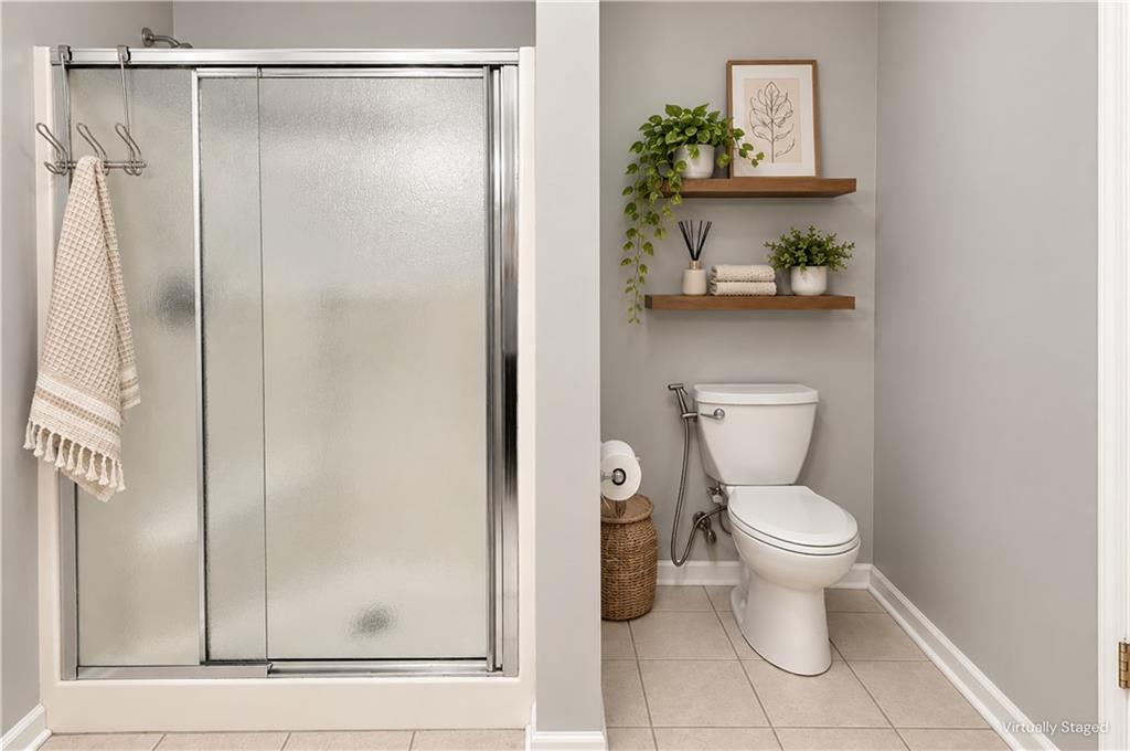Bathroom with a frosted-glass shower and toilet beneath floating shelves with plants and towels.