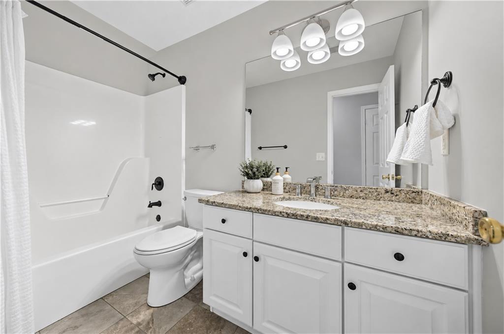 Bathroom with a white tub and shower beside a granite-topped vanity and large mirror.