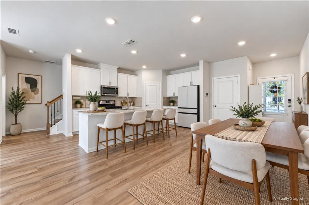 Open kitchen and dining area with a white island, wood floors, and staged furnishings.