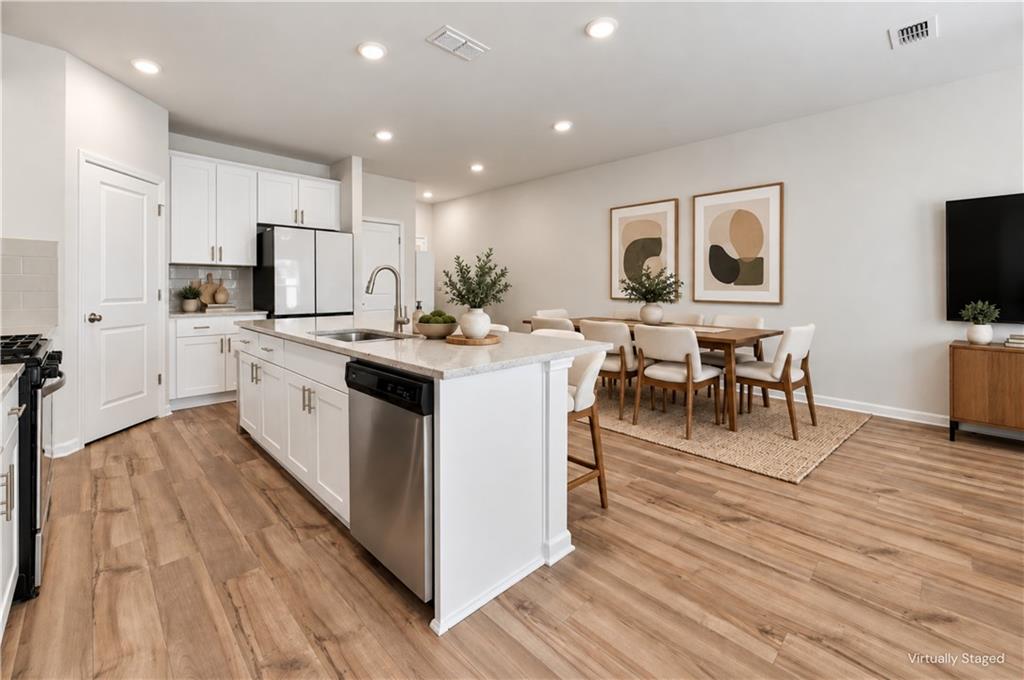 Kitchen and dining area with a large island, white cabinetry, and wood-look flooring.