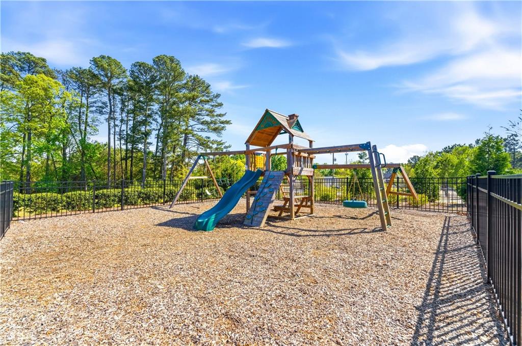 Fenced outdoor playground with a wooden play structure, slides, and climbing wall.