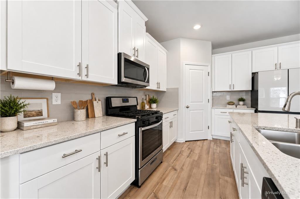 Bright kitchen with white cabinets, speckled countertops, stainless appliances, and wood-look flooring.