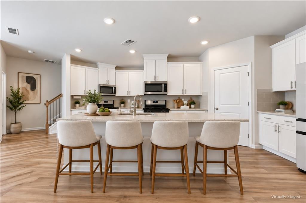 Virtually staged kitchen with white cabinetry, a large island, and four upholstered bar stools.
