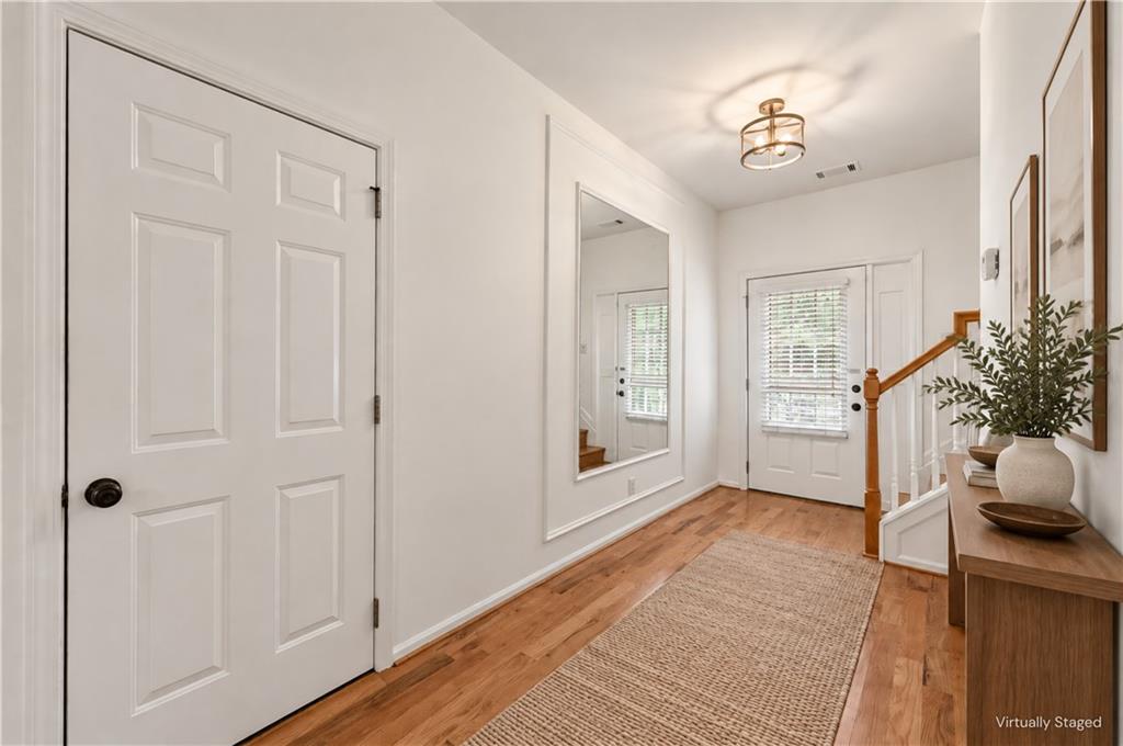 Entry foyer with hardwood floors, a woven runner, and a staircase with a wood handrail.