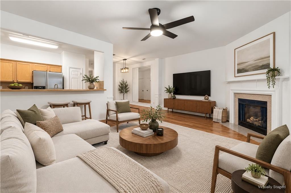 Virtually staged living room with a white sectional, fireplace, and open kitchen.