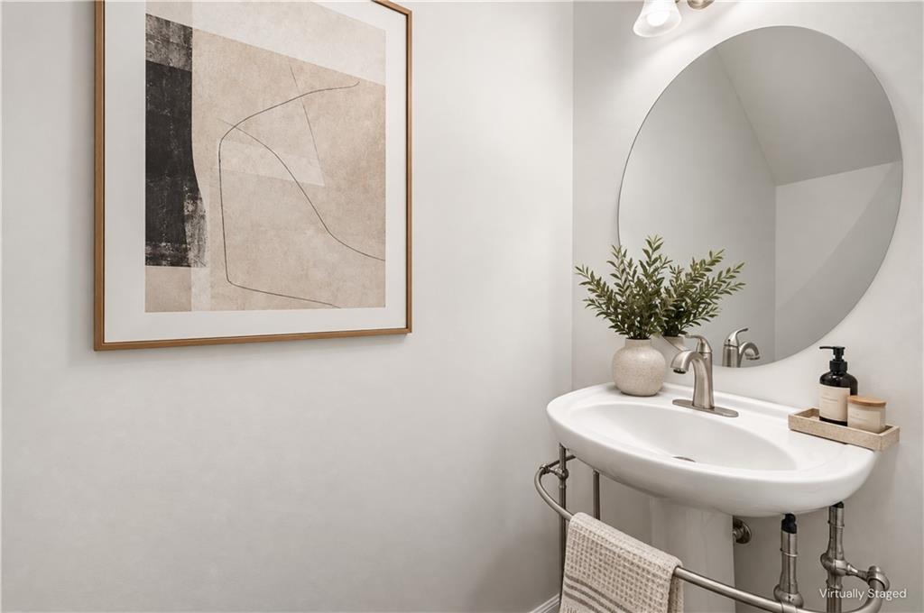 Bathroom vanity with a white pedestal sink, round mirror, and framed abstract artwork.