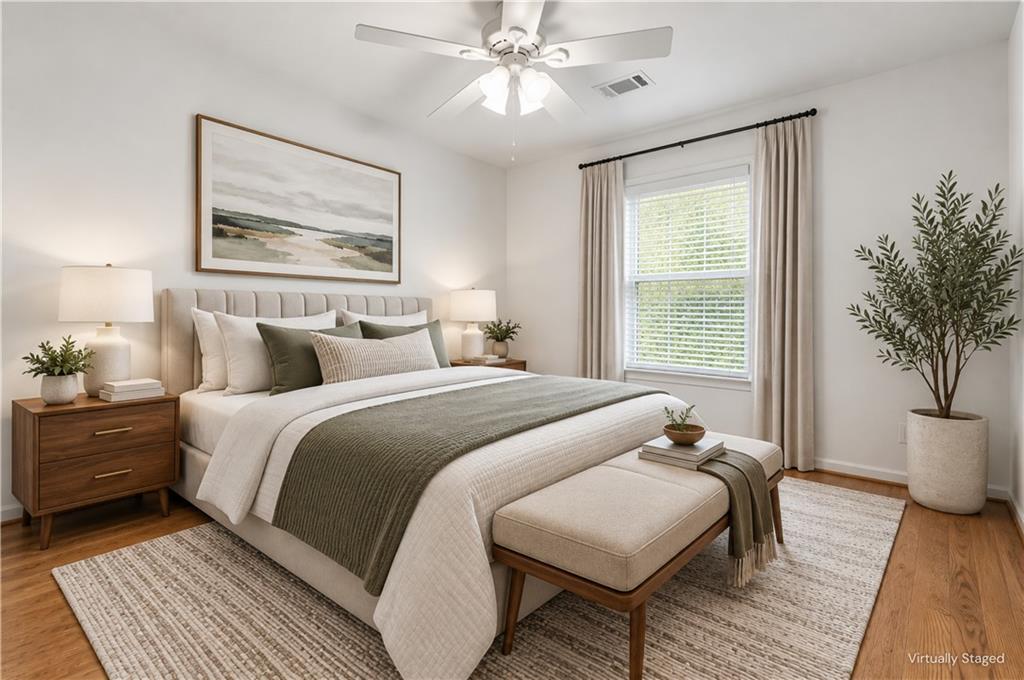Virtually staged bedroom with a large upholstered bed, neutral bedding, wood nightstands, and a potted tree.