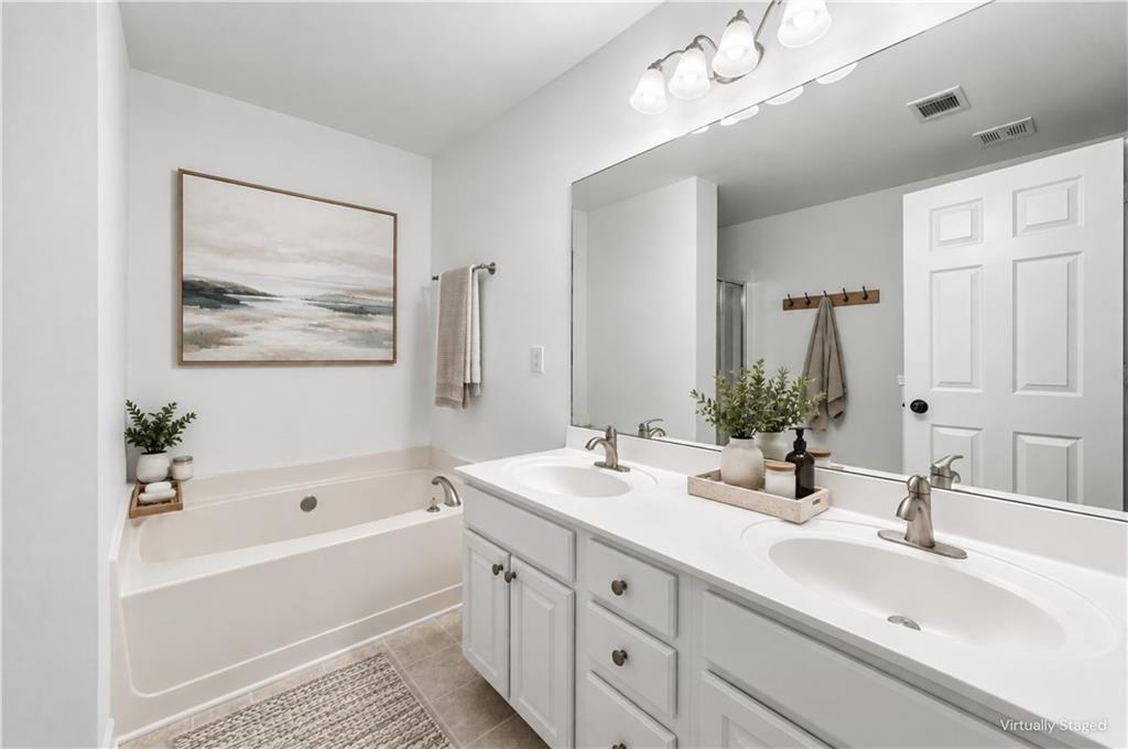 Bright staged bathroom with a bathtub, double-sink vanity, and large mirror.