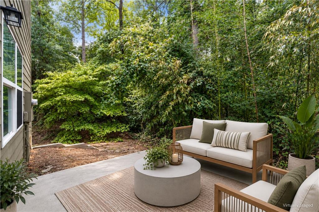 Outdoor patio with a staged sofa and chairs, round coffee table, and dense greenery.