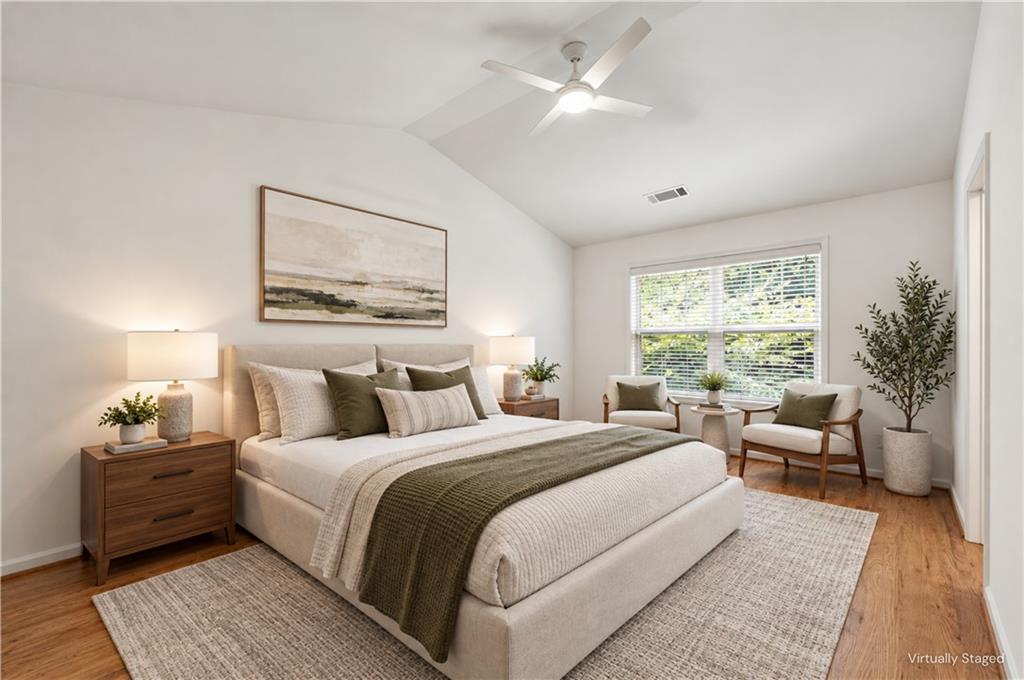 Virtually staged bedroom with a large upholstered bed and a window-side sitting area.