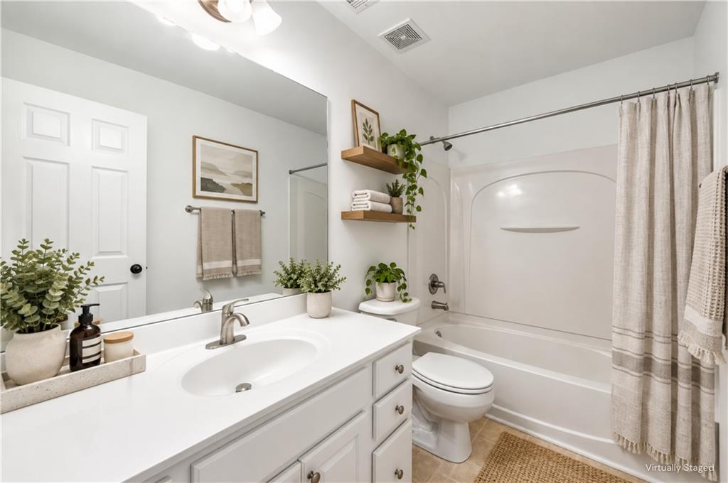 Bathroom with a white vanity and sink, bathtub with shower curtain, and decorative plants.