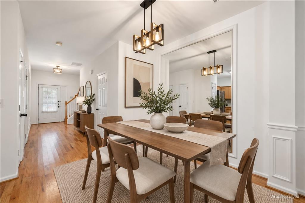Dining room with a long wooden table, upholstered chairs, and geometric pendant lights beside a hardwood entry hall.